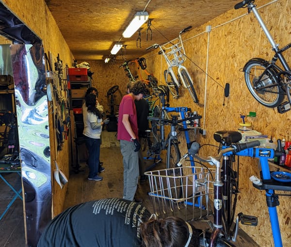 Three people inside a workshop with bikes on stands looking over their components.