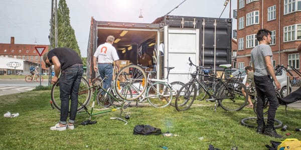 Three people working on their bikes overturned in from of the workshop outside.